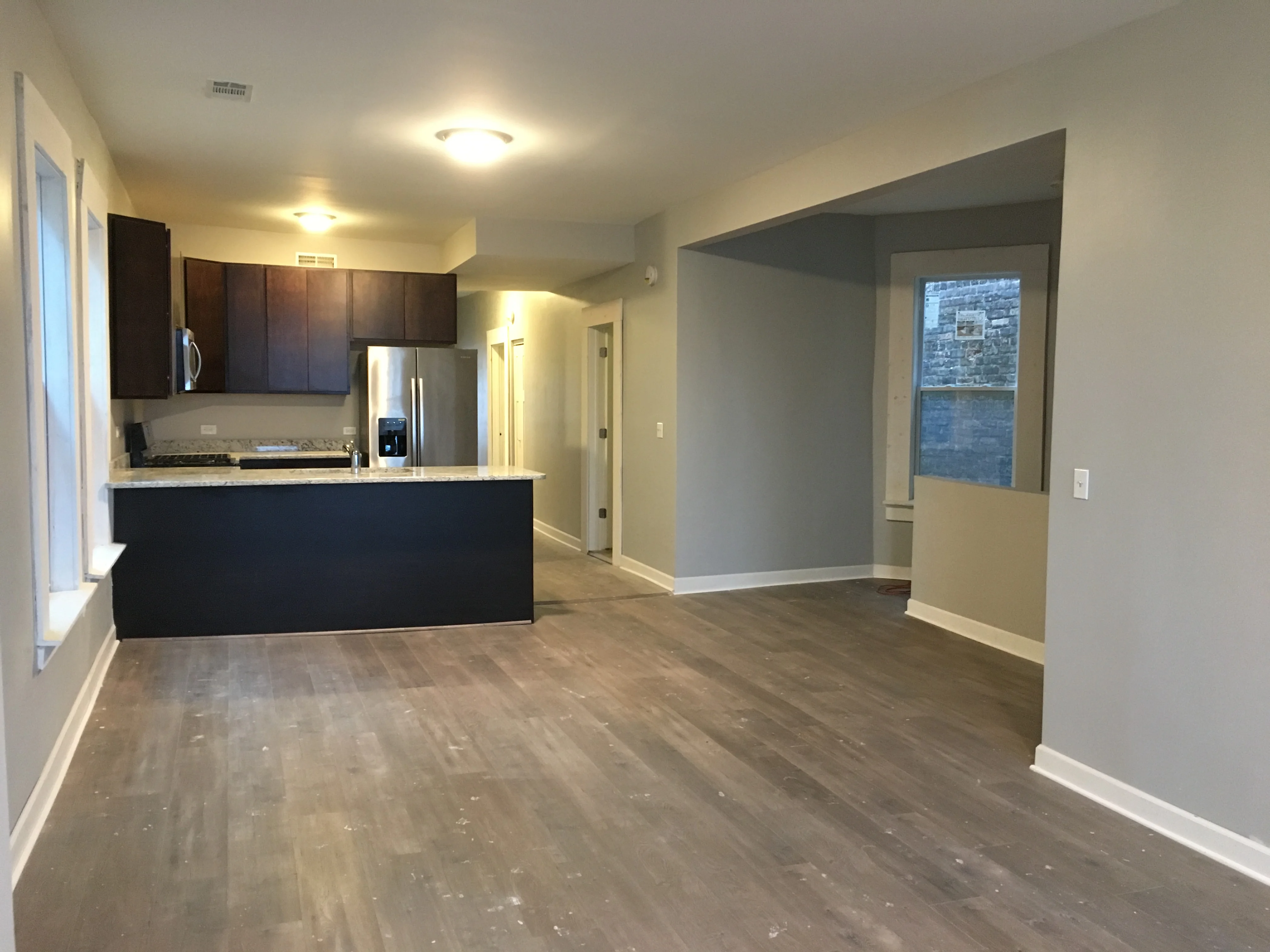Modern kitchen with dark cabinets, stainless appliances, and open living area with hardwood floors