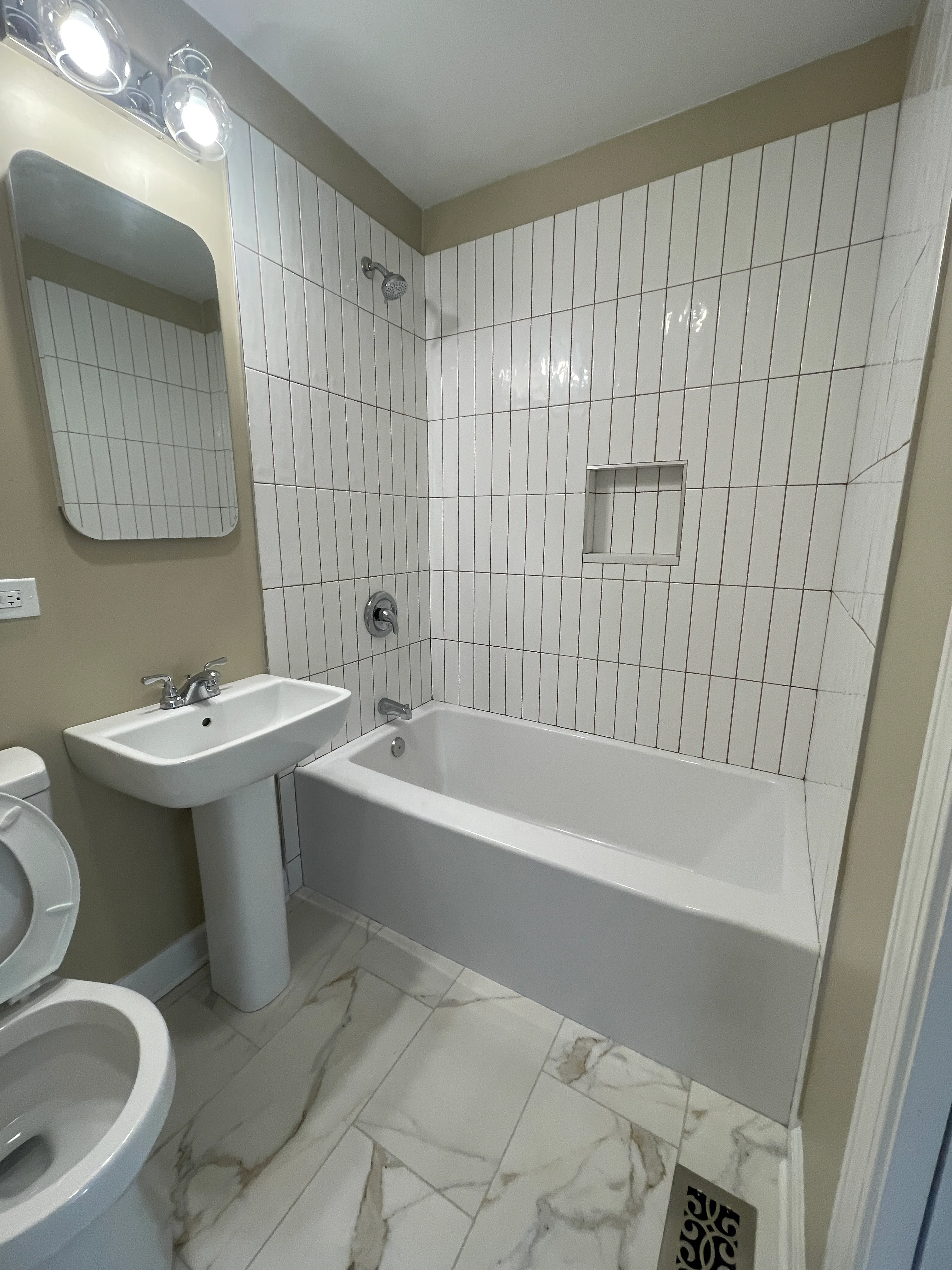 Renovated bathroom with white subway tile walls, pedestal sink, and marble-look flooring