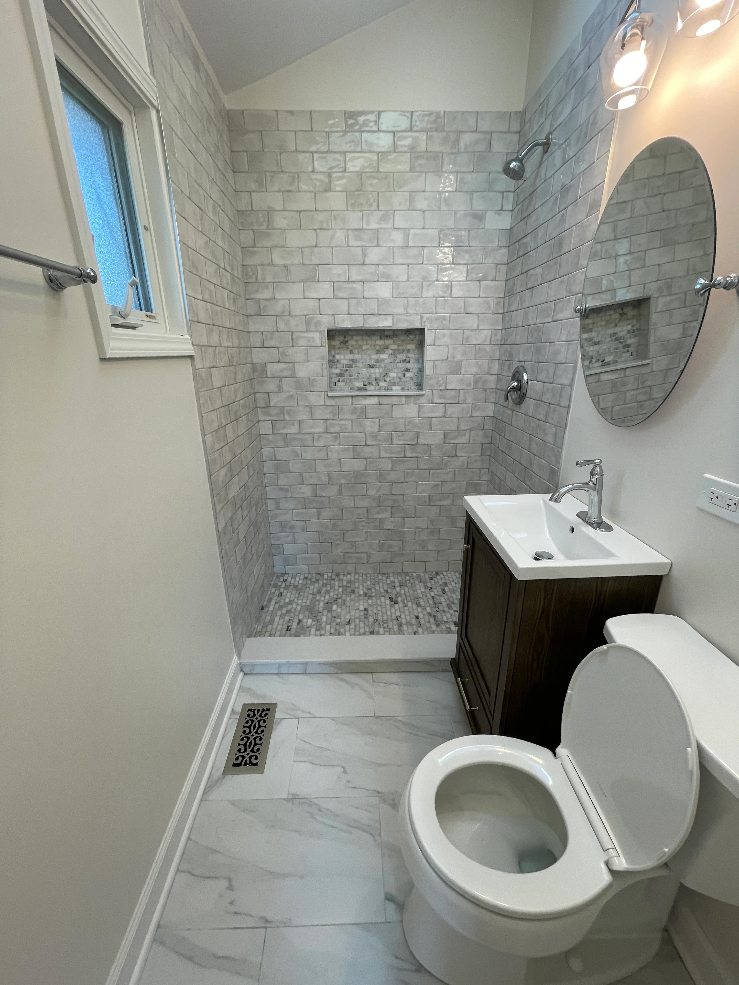Modern bathroom with gray subway tile shower, dark vanity, and marble flooring