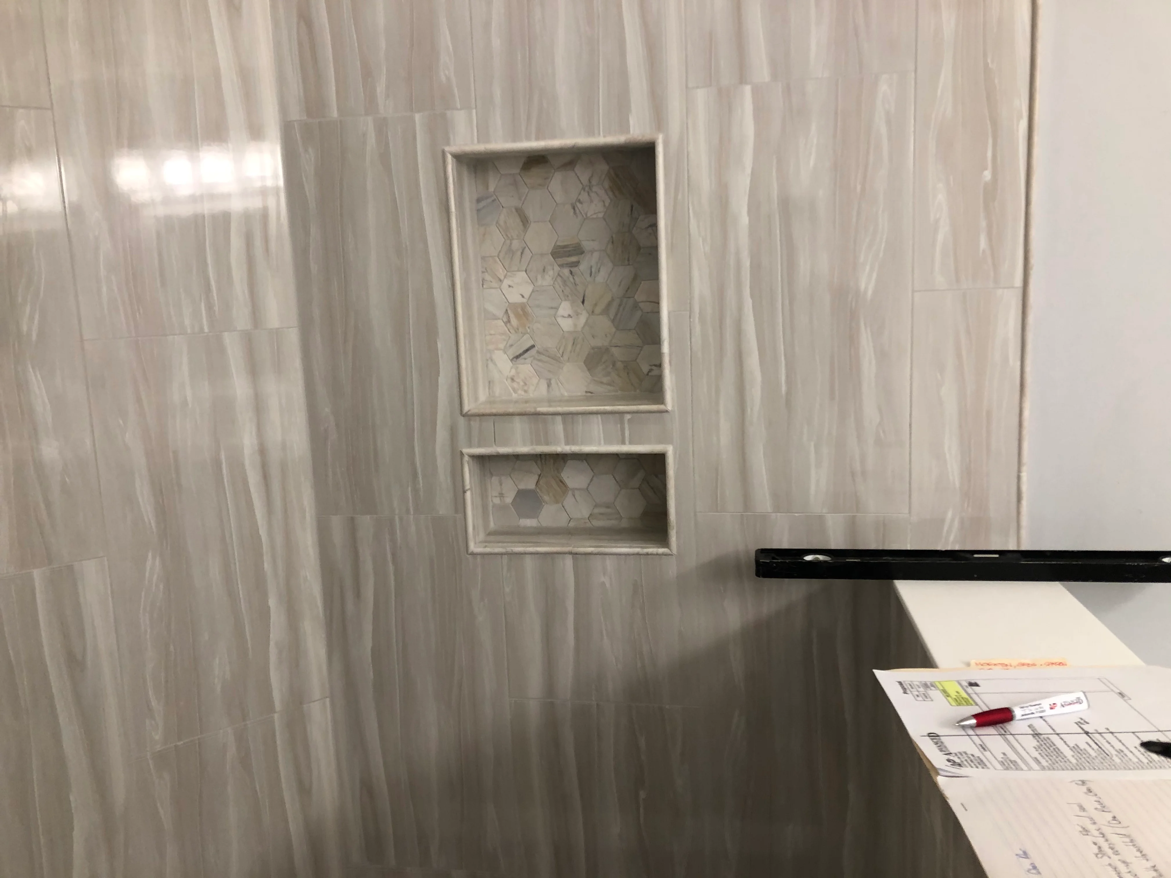 Bathroom shower wall with gray linear tile and two recessed shelves with hexagonal tile inserts