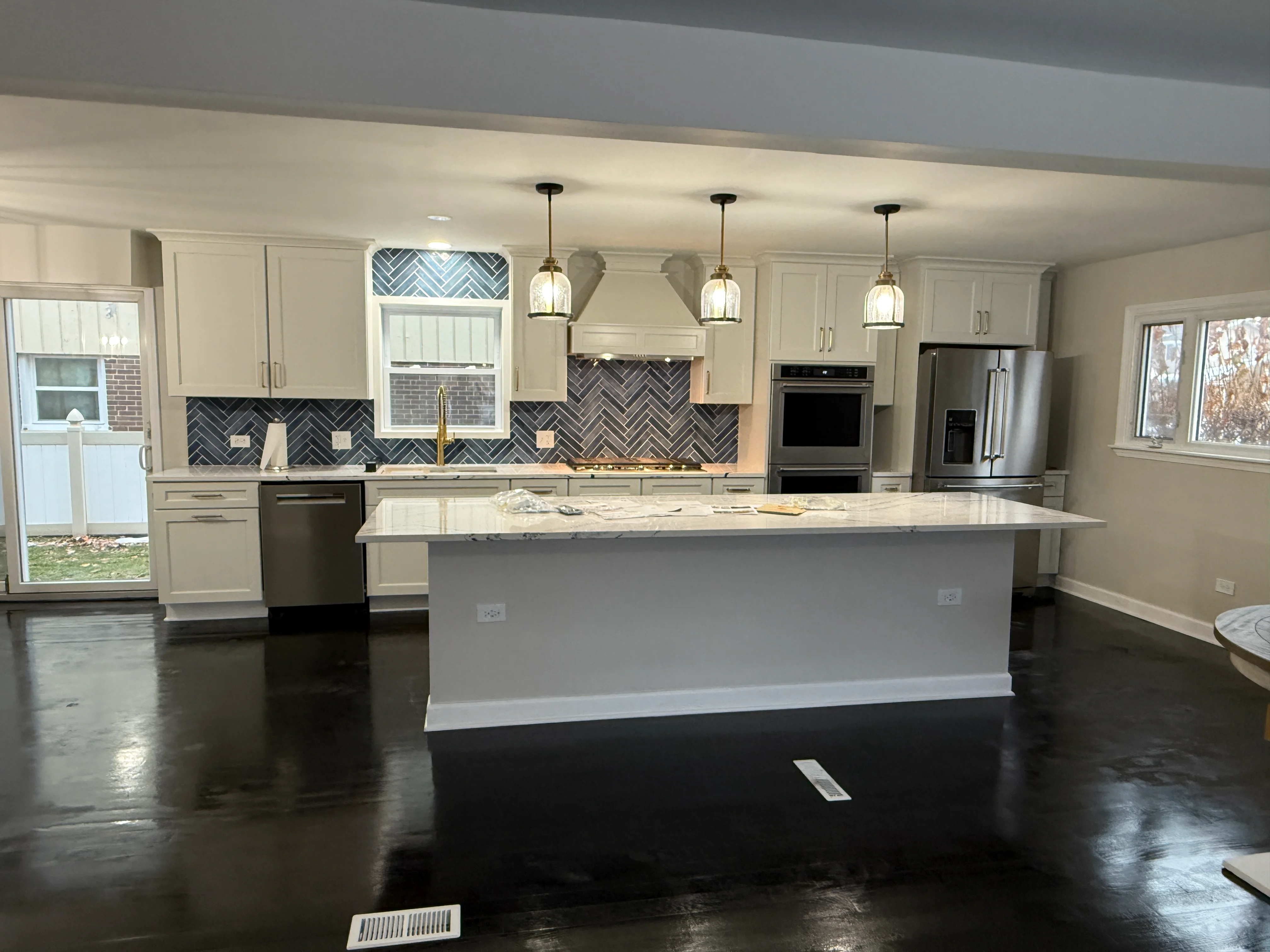 Modern kitchen with cream cabinets, gray herringbone backsplash, and large white quartz island