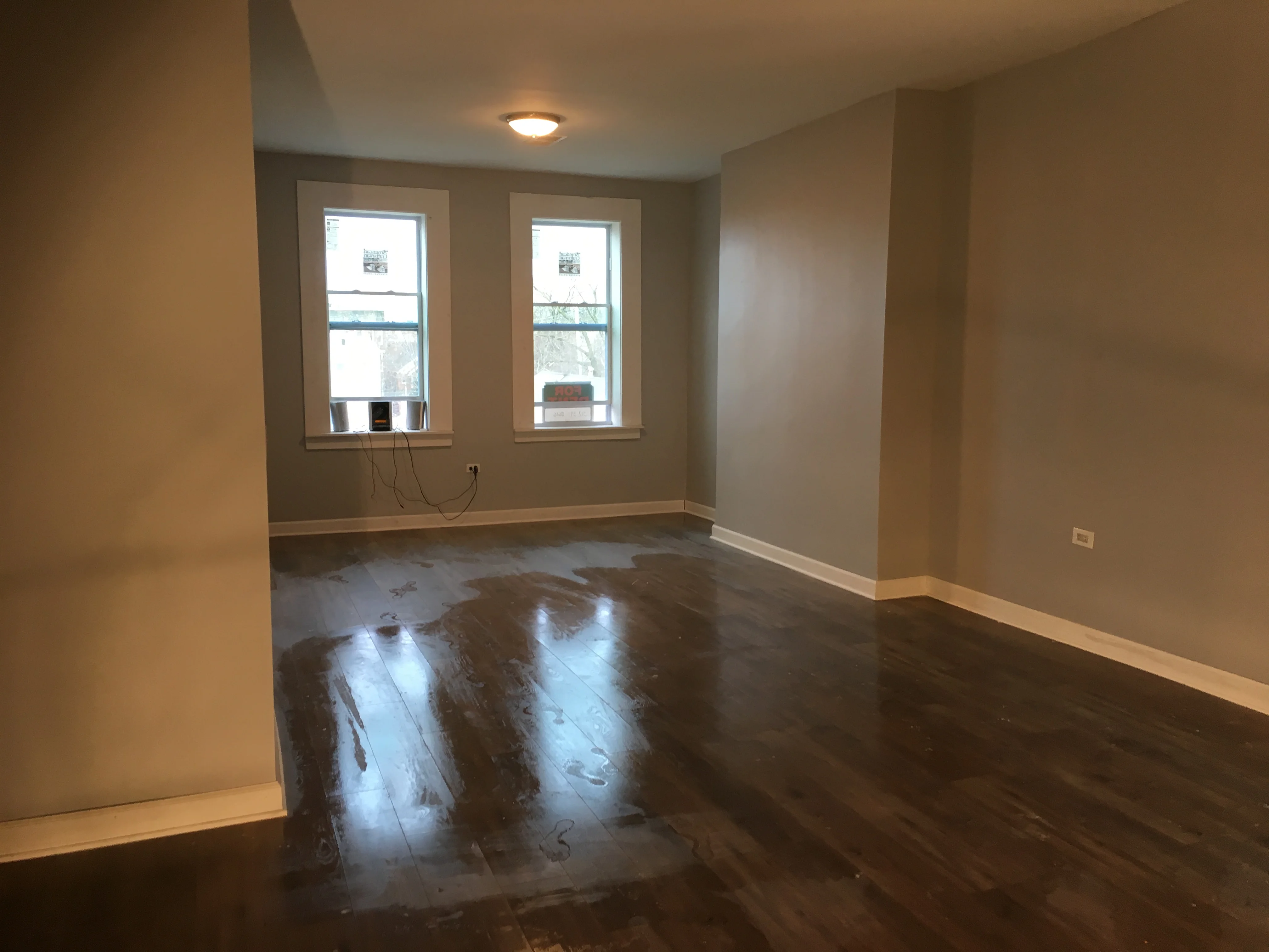 Newly renovated room with dark hardwood floors, neutral walls, and two large windows