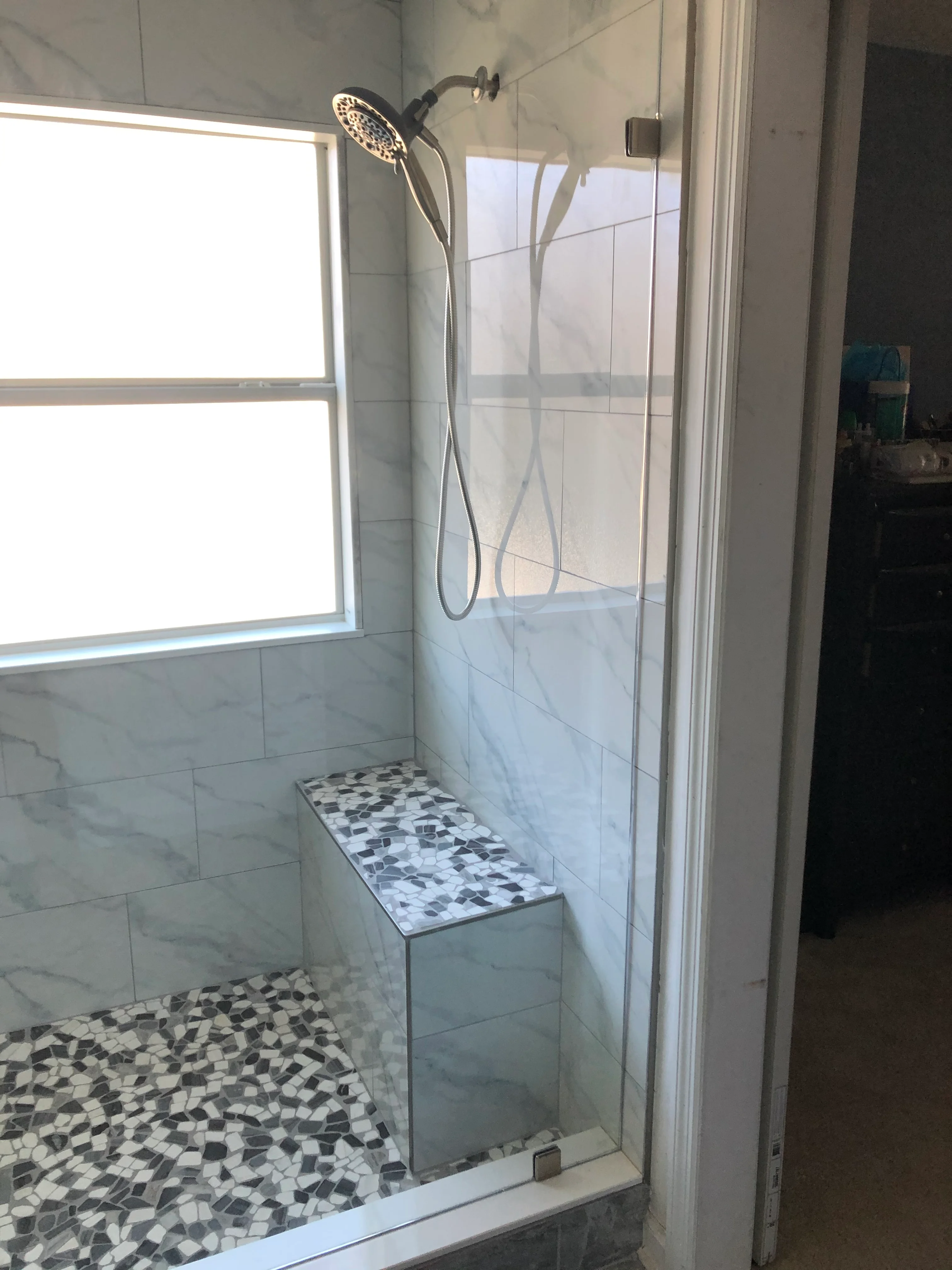 Modern bathroom shower with marble tile walls, mosaic floor, and frameless glass enclosure