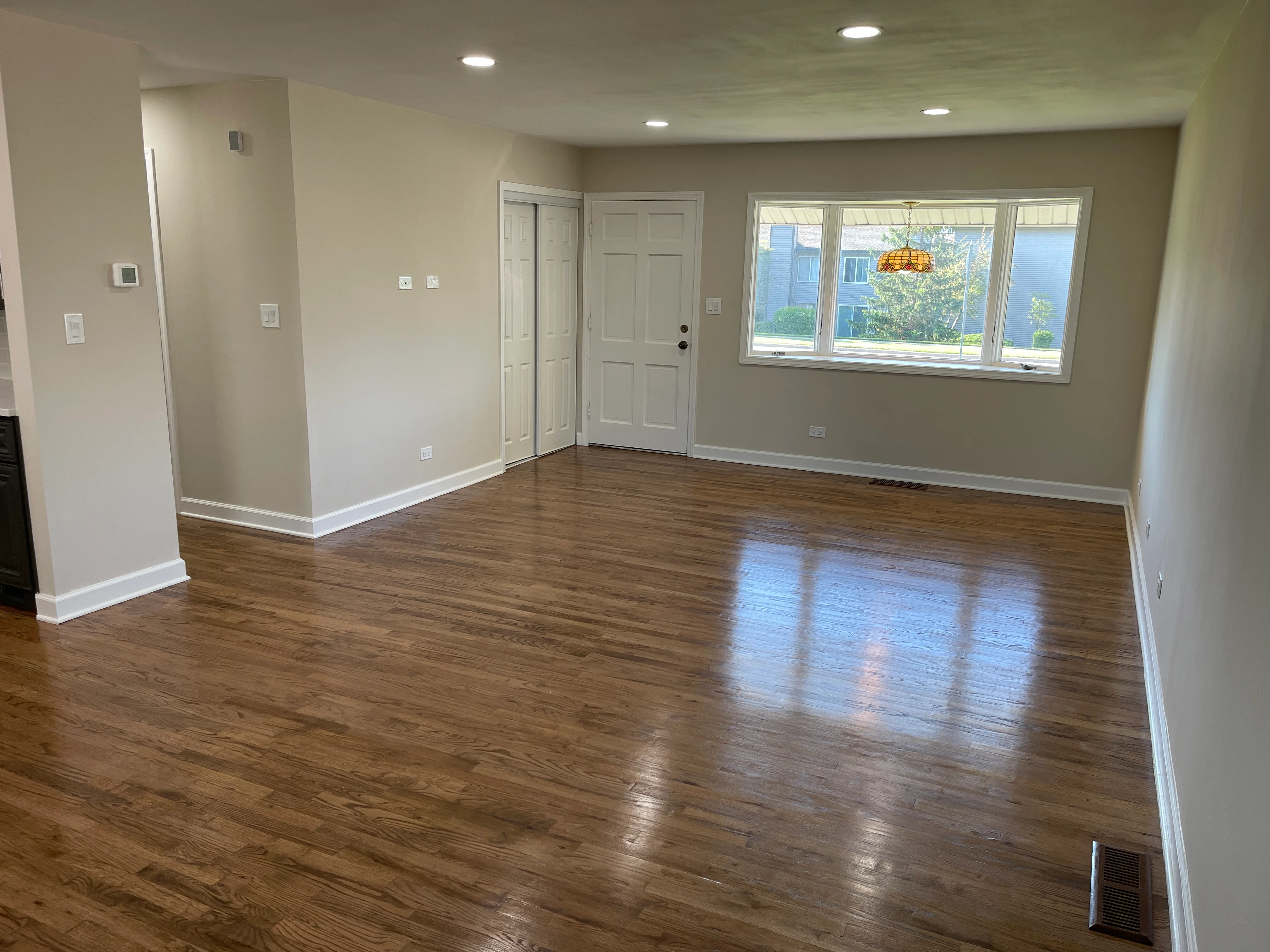 Spacious open concept room with hardwood floors, neutral walls, white trim, and large windows