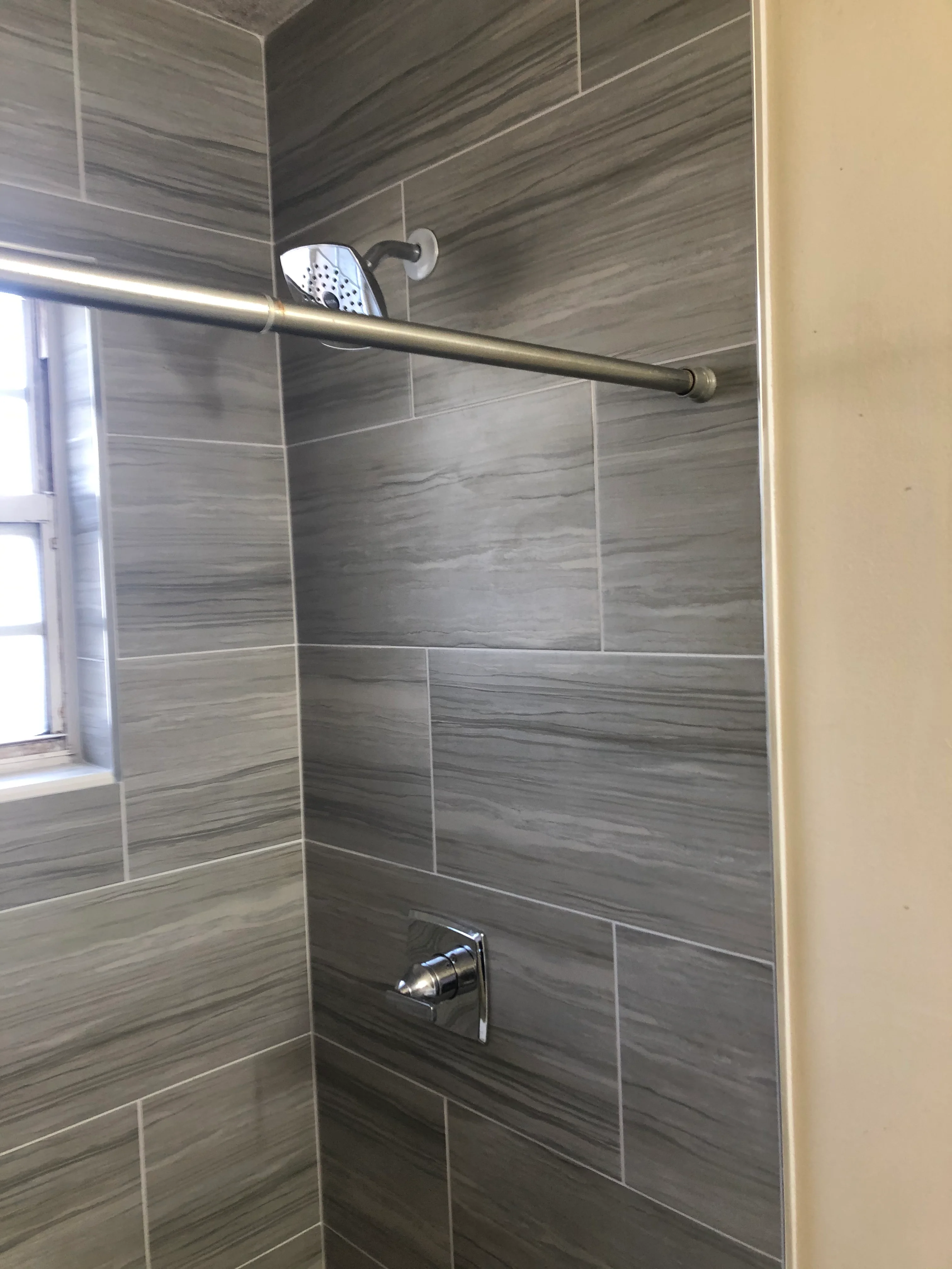 Gray wood-grain tile shower with brass rod and chrome fixtures